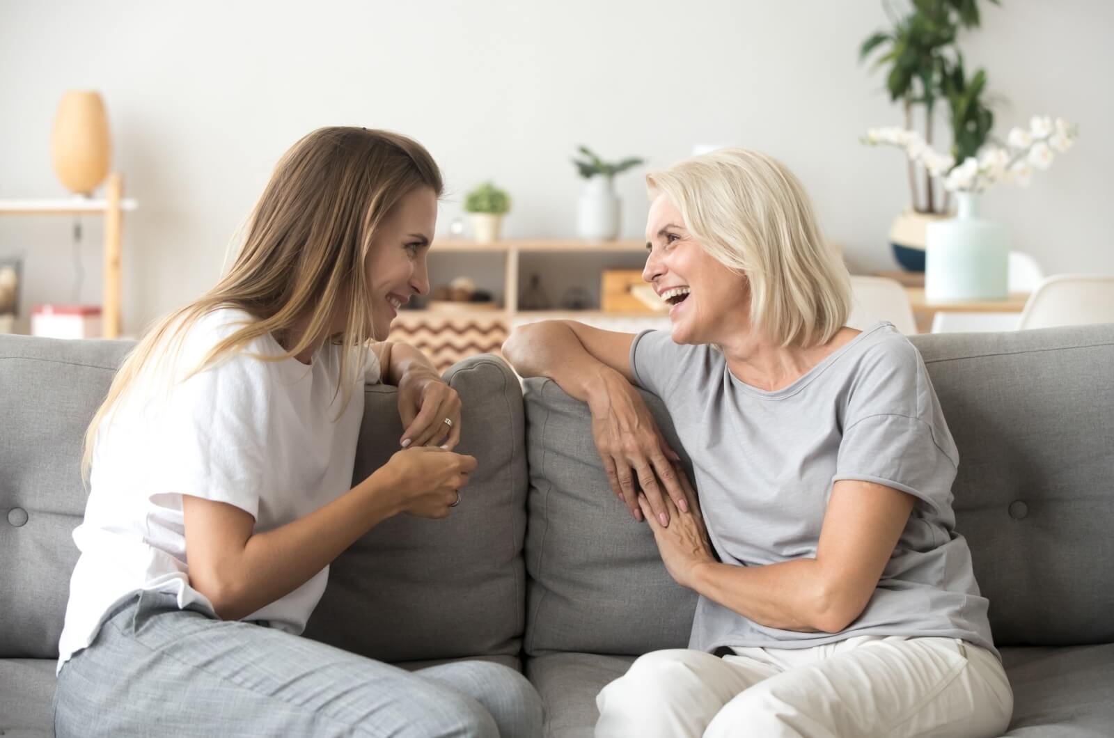 An adult child and their parent sitting on a couch laughing and talking.