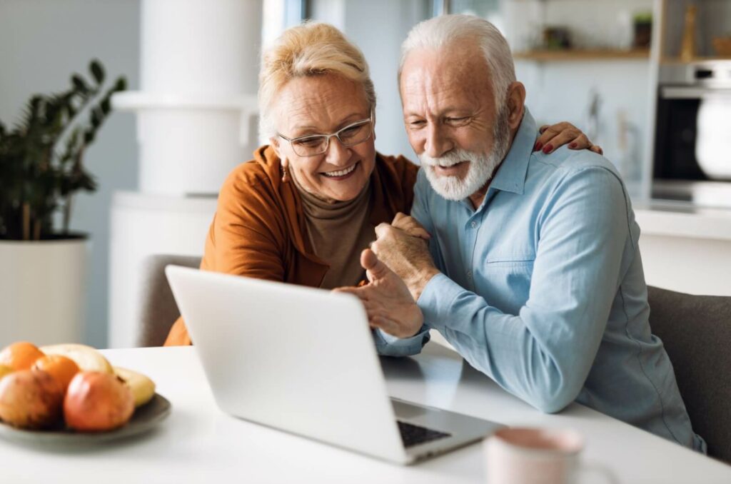 An older couple at home in front of the laptop, excitedly looking at independent communities and hugging.