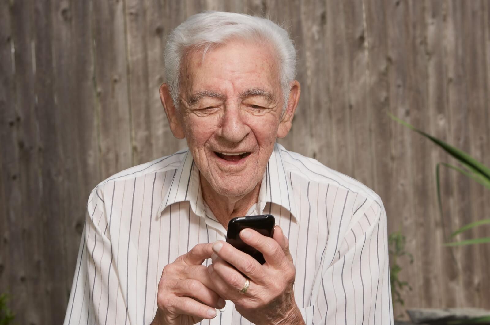 An older adult man smiling and holding a smartphone