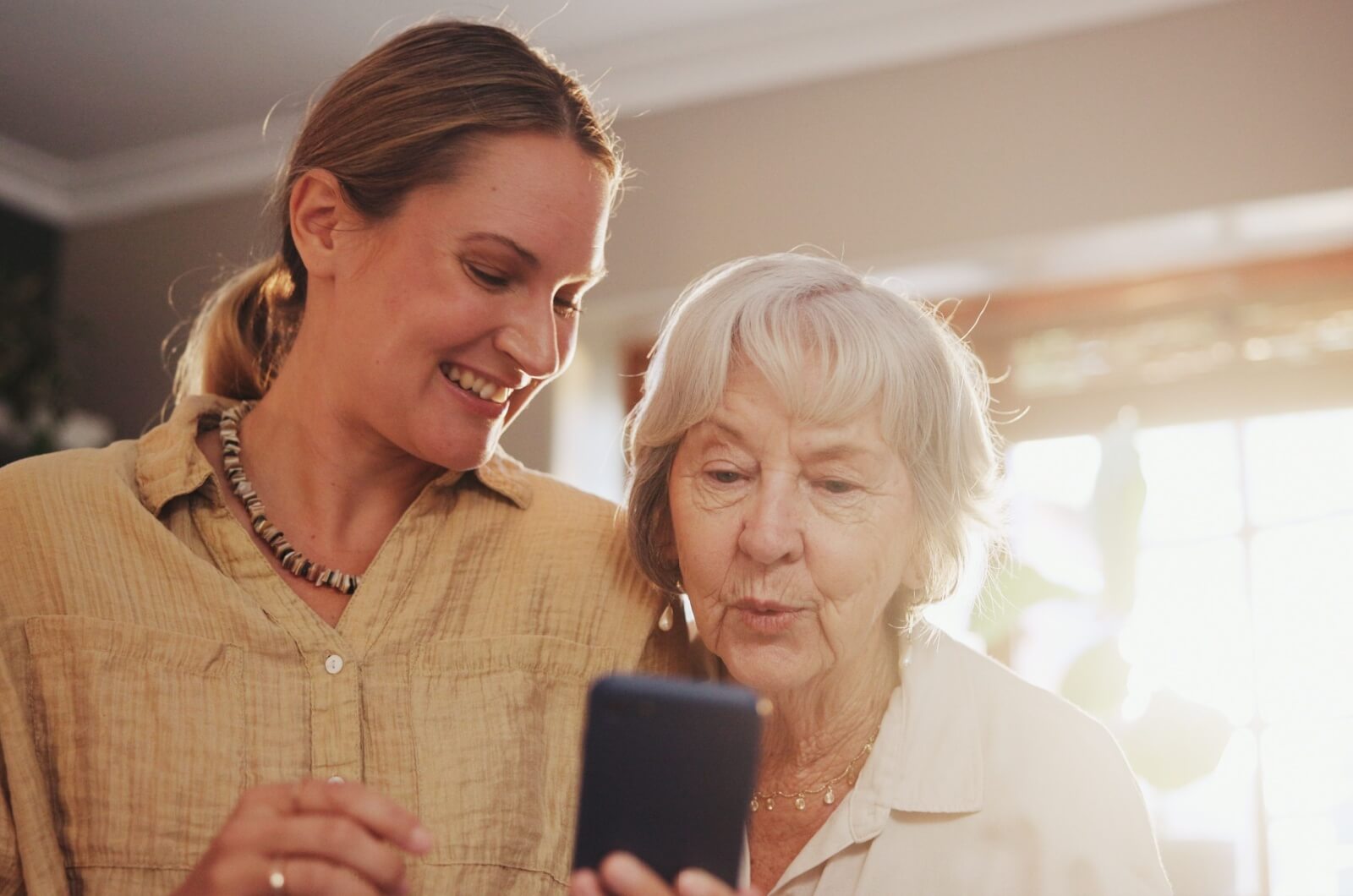 An adult child showing a parent with dementia something on the phone.