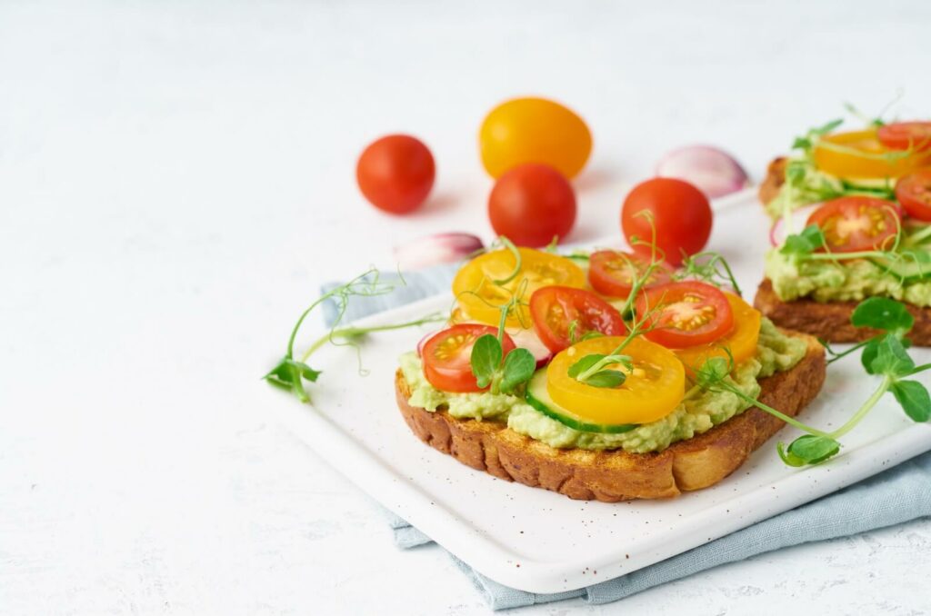 A plate of avocado toast with tomatoes on top against a white background.