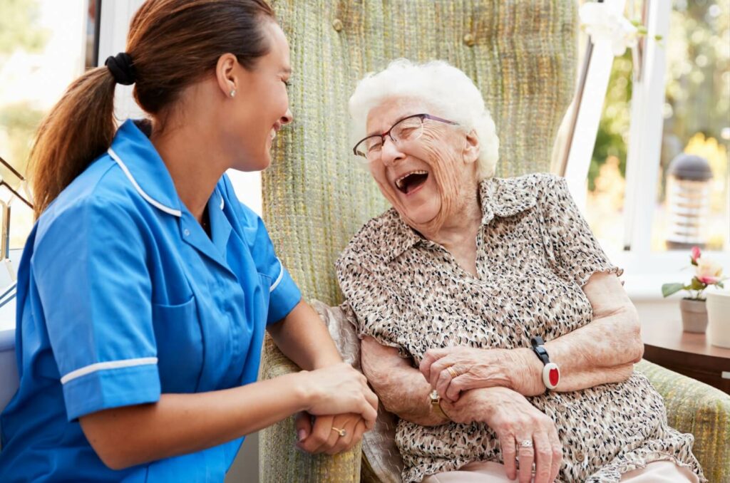 A senior resident and on-site nurse sit together outside sharing a laugh.