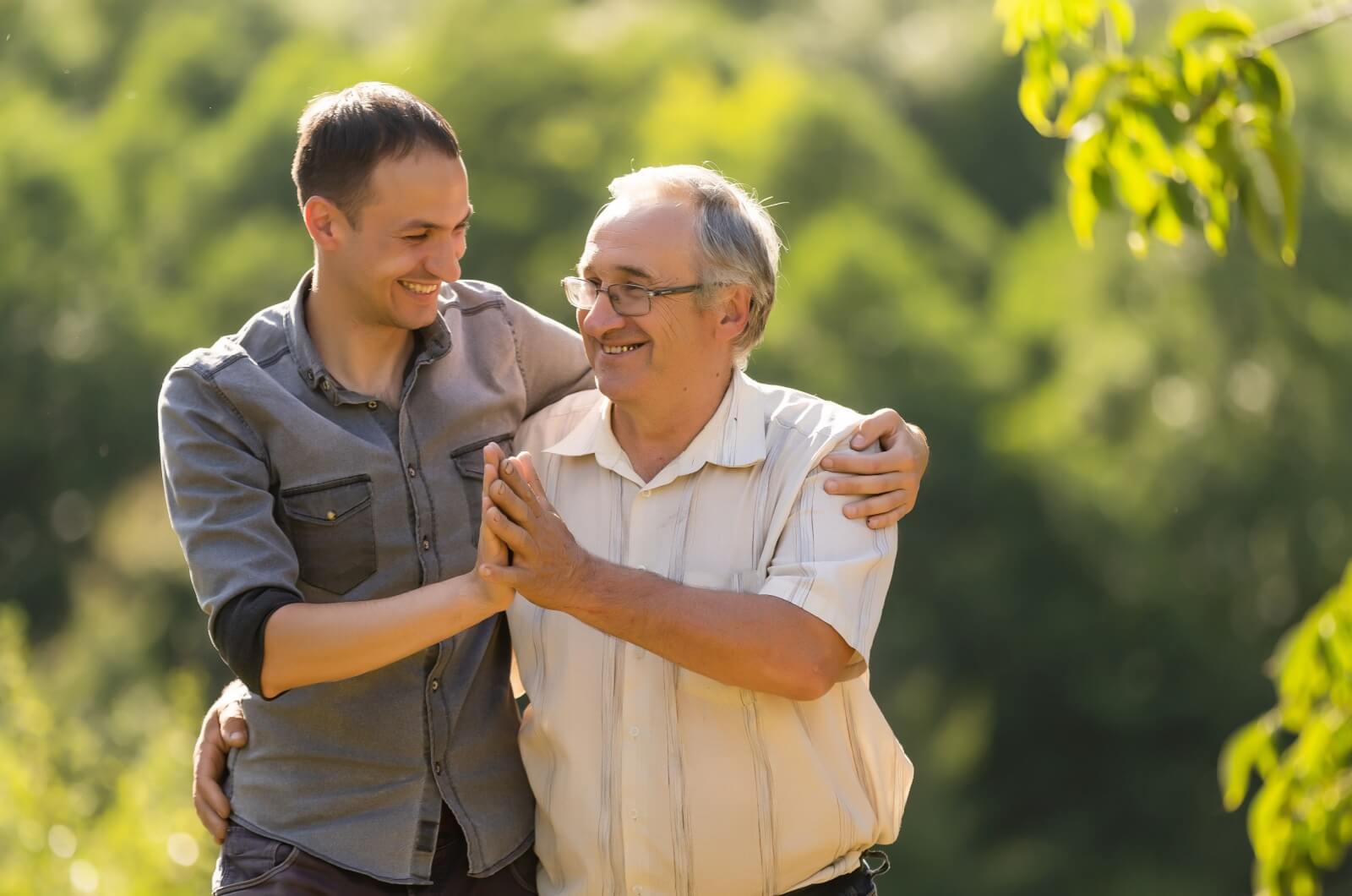 A senior and his adult son smile at each other as they enjoy a walk together.