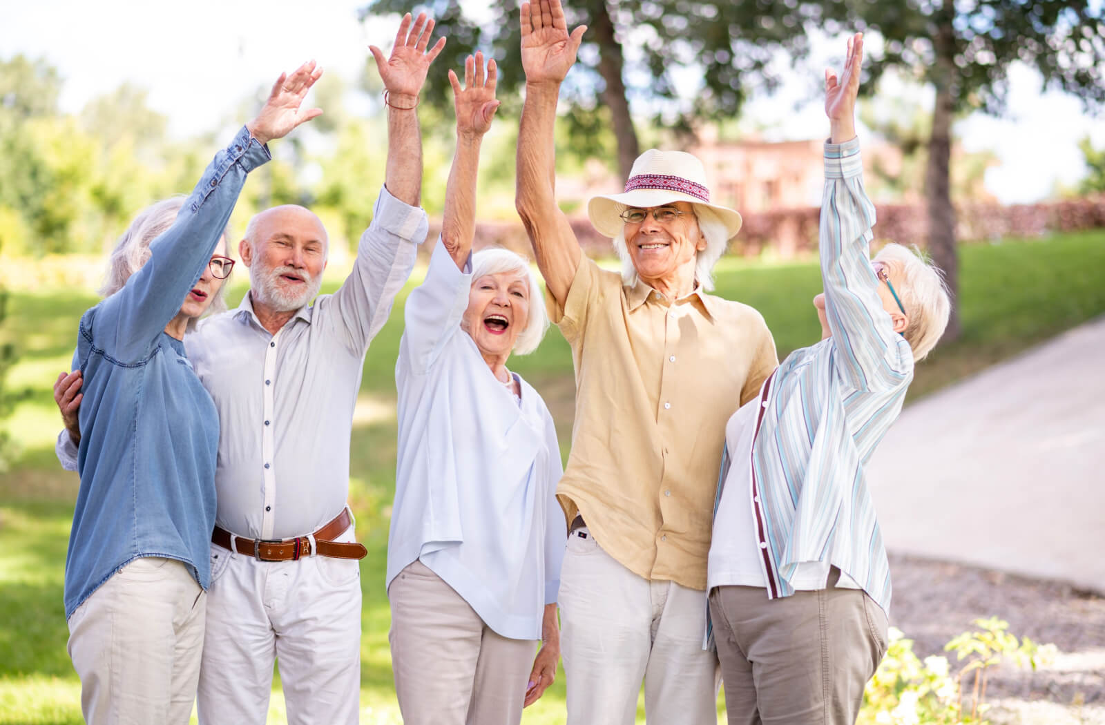 A group of older adults laughing in the park and waving their arms overhead.
