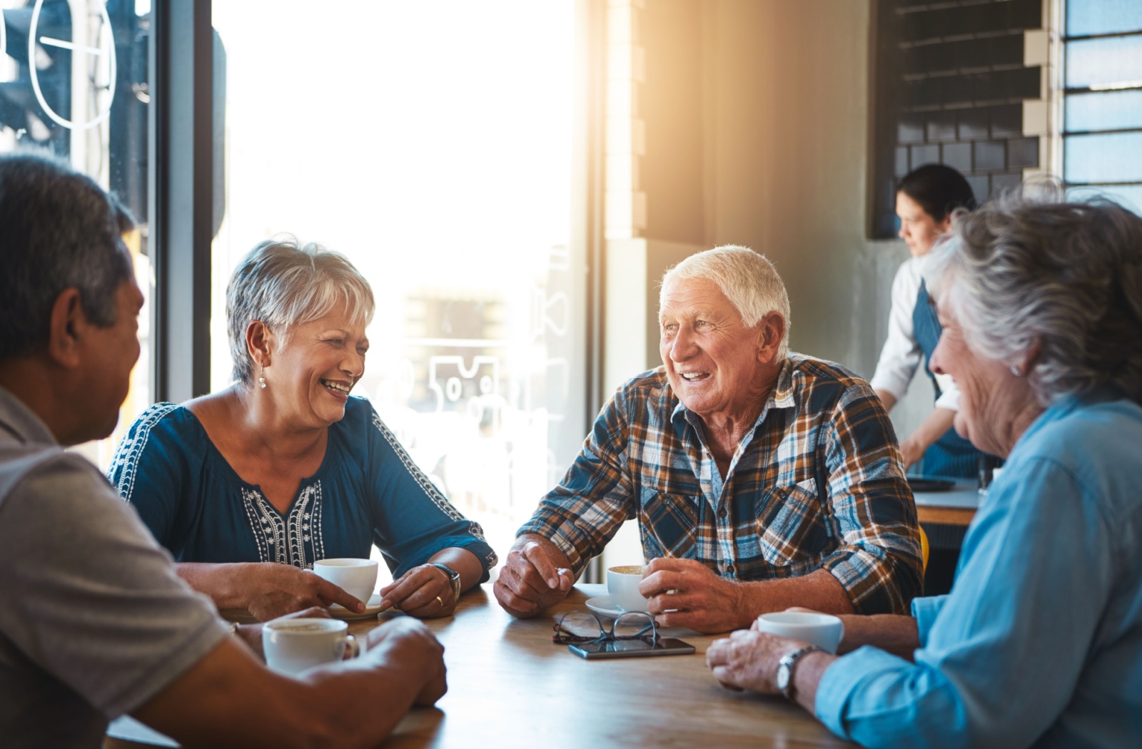 A group of older friends in senior living sitting around a sunlit table in a cafe in senior living.