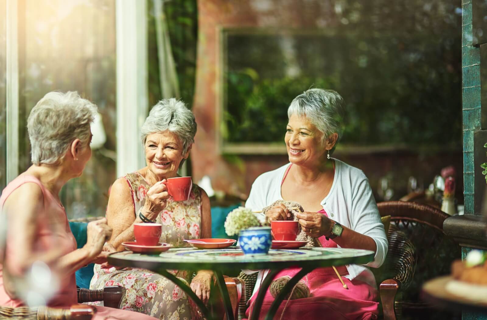 A small group of senior sits around drinking a tea and chatting in their community common area.