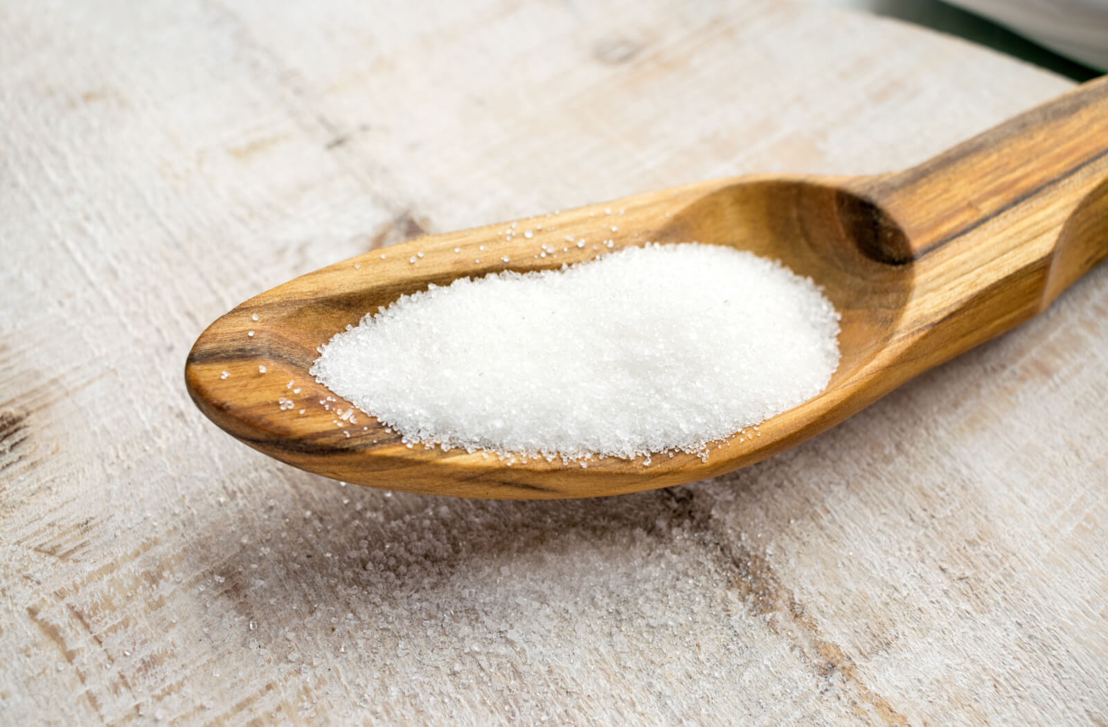 A close-up image of powdered artificial sweetener resting on a wooden spoon.