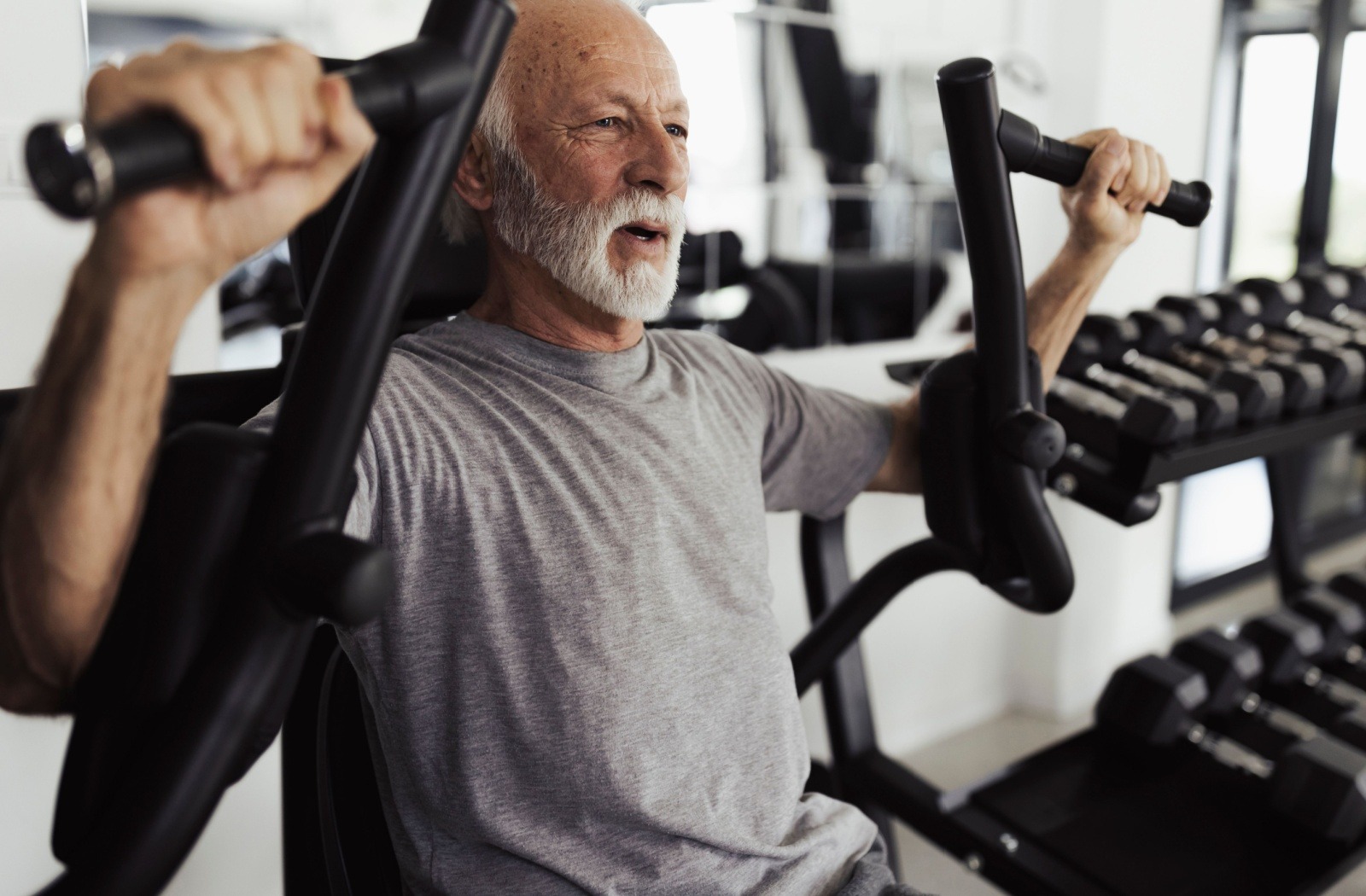 A senior works out in a gym using a shoulder press weight machine.