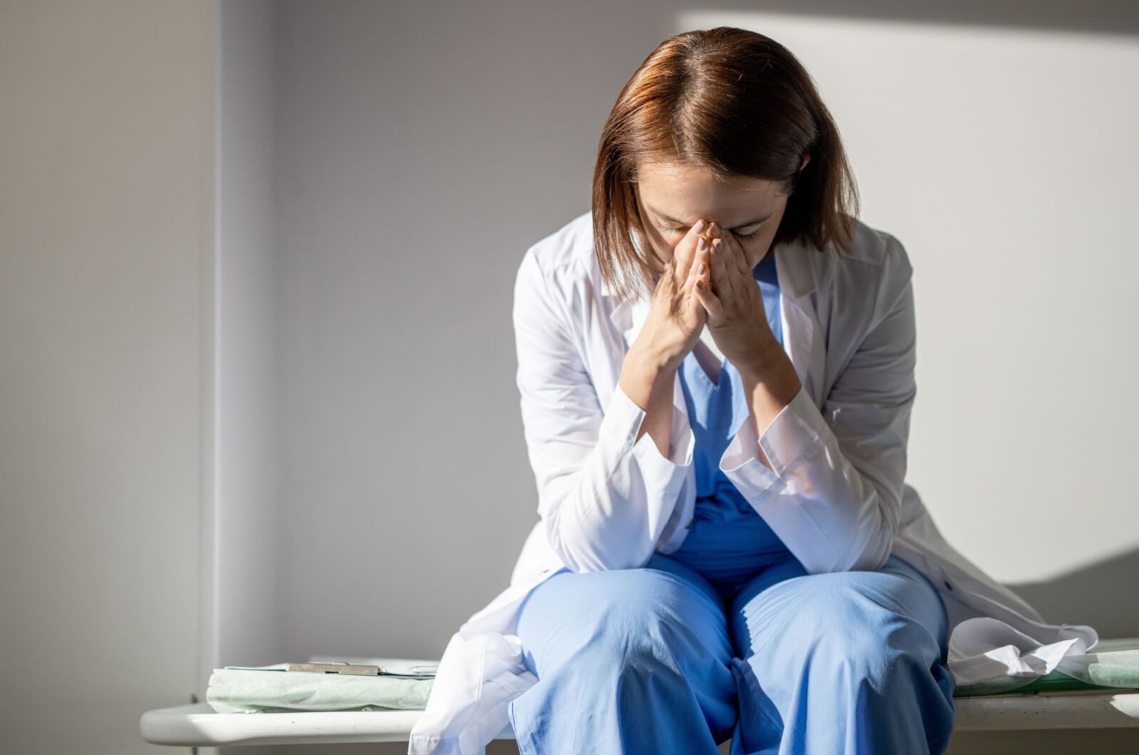 The frustrated female caregiver in uniform sits on a bench, her hands touching her forehead with a sense of weariness.