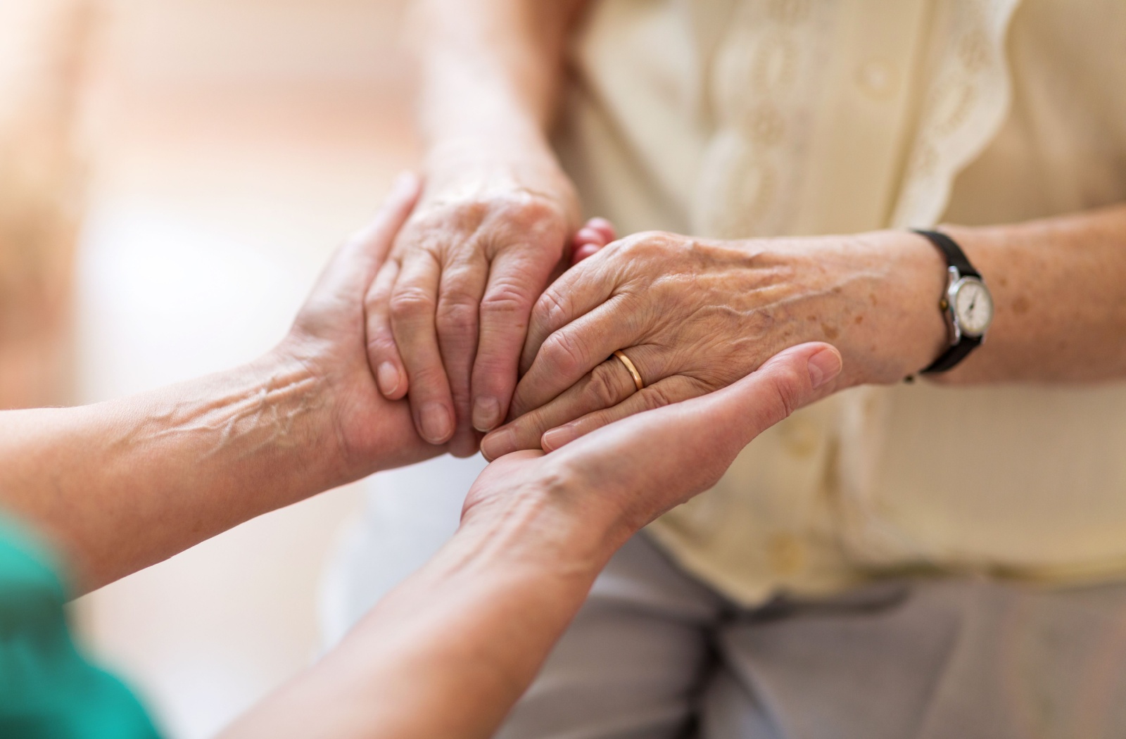 A senior residing in memory care holds the hands of a caregiver.